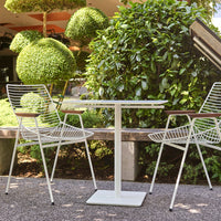"White metal outdoor table with striped chairs amid lush greenery and neatly trimmed hedges."