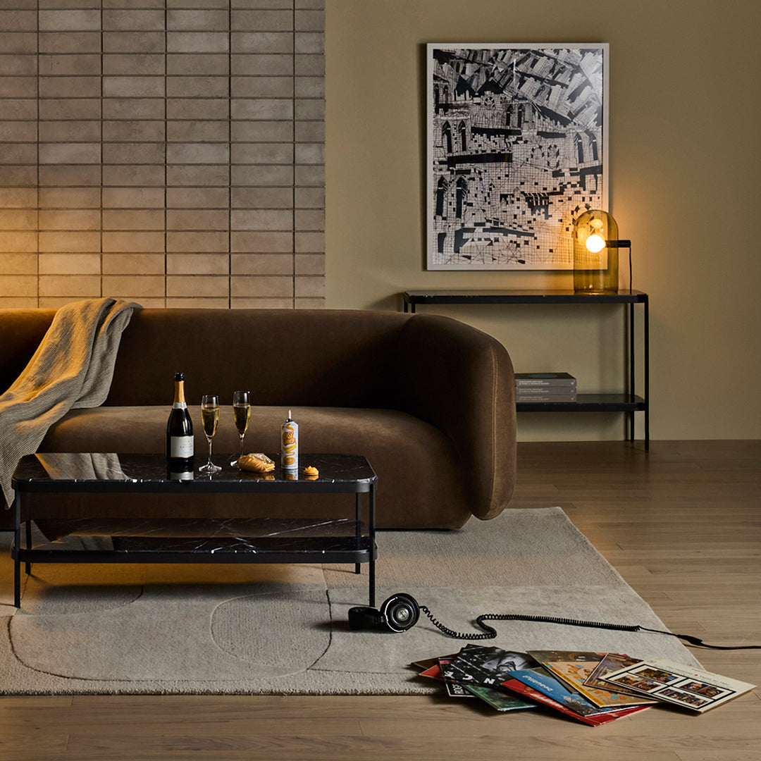 Brown modern sofa with textured beige throw, contrasting black glass coffee table, and soft gray area rug.