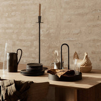 Elegant rustic dining setup with black plates, natural wood tones, and earthy textures against a neutral background.