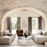 Beige sectional sofas with plaid and solid throw pillows, complemented by earthy tones and rustic stone walls.