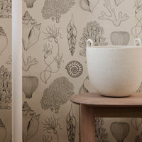 Beige wallpaper featuring detailed illustrations of coral and sea plants in natural tones, complemented by a light-colored planter.