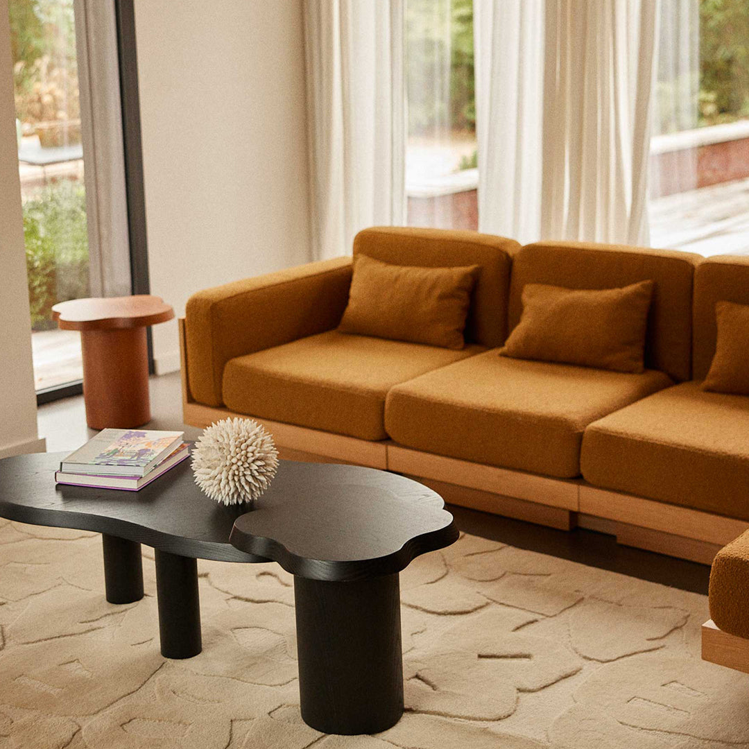 Rust-colored couch with plush cushions, complemented by a black organic-shaped coffee table and neutral beige rug patterns.
