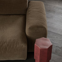 Brown velvet sofa with a plush texture and a contrasting red hexagonal side table against a dark wood floor.