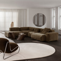 Lush olive green sectional sofa in a modern living room with a round beige rug and sleek, dark wood accents.