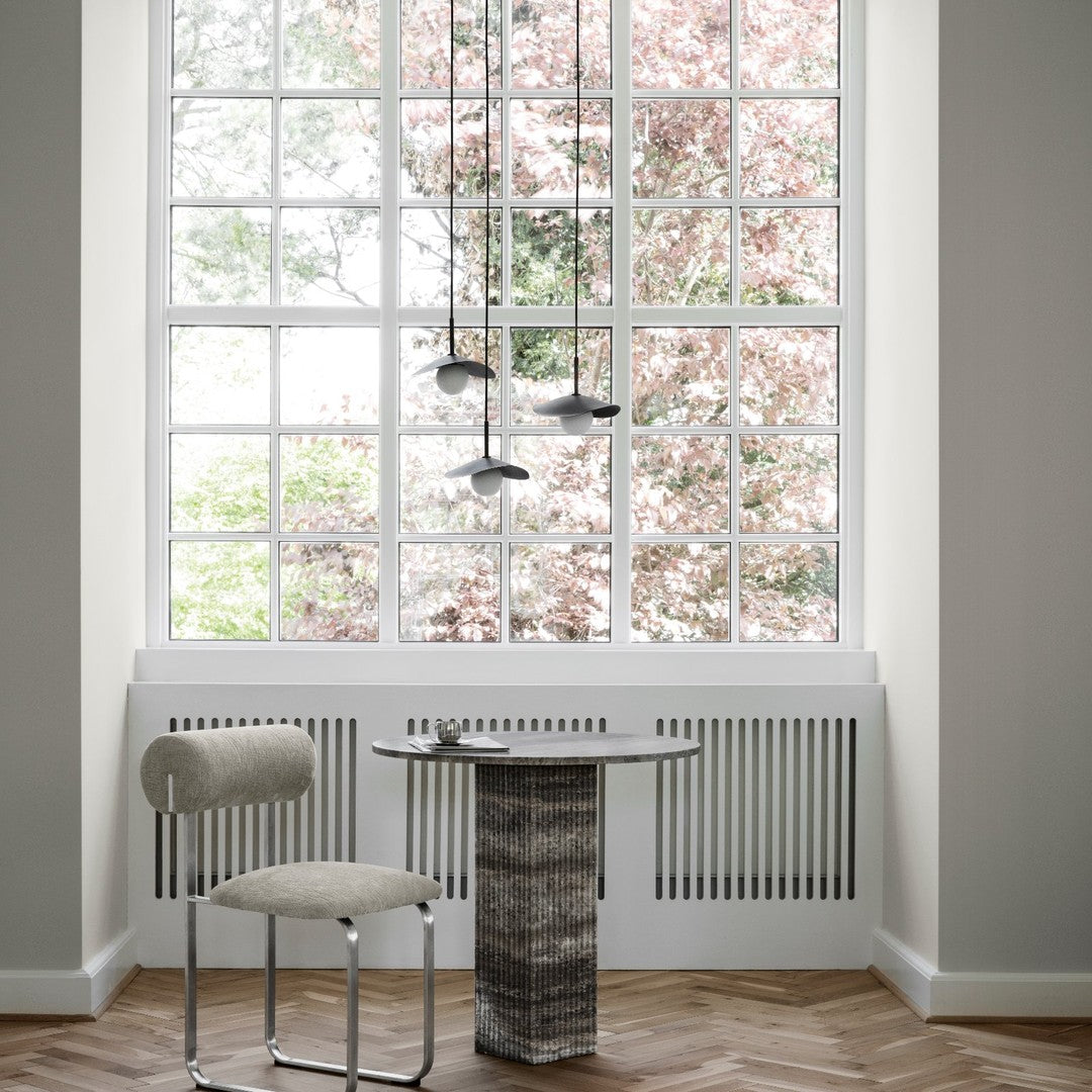 Modern gray chair with cream upholstery beside unique textured black and white table, set against a light-filled window.