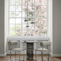 Minimalist dining area with soft gray tones, warm wood flooring, and contemporary patterned chairs against a bright window view.