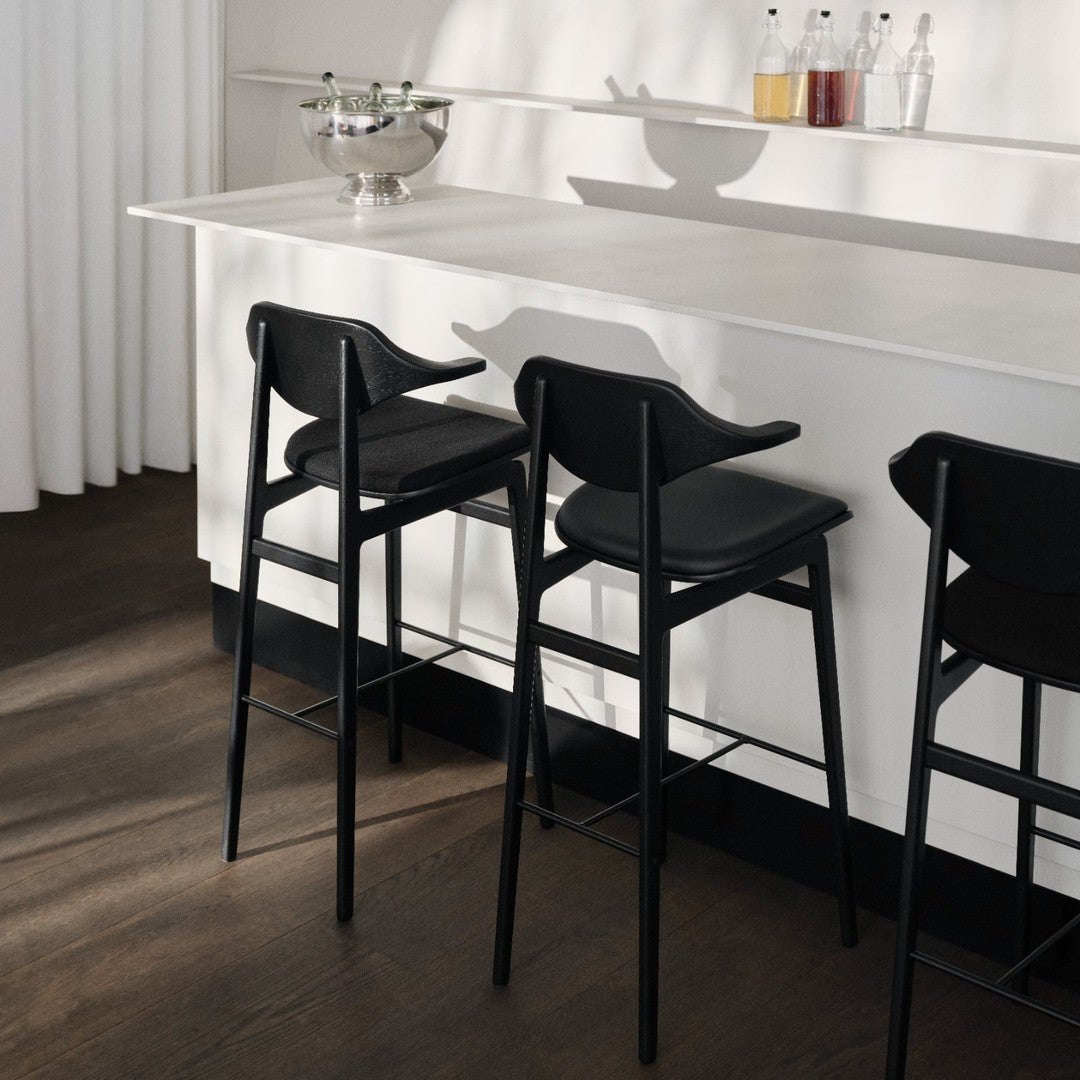Black bar stools with sleek lines against a minimalist white countertop and warm wood flooring.