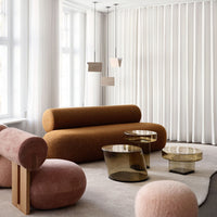 Modern living room with a rust-colored sofa, pink accent chairs, and glass tables, featuring neutral tones and soft textures.