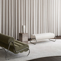 Green textured chair and sleek white bench against soft, neutral curtains and a light rug. Modern, minimalist design.