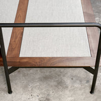 Wooden table with a sleek natural finish, featuring a light gray linen inset and sturdy black metal legs.