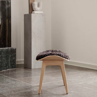 Grey textured seat cushion on a light wood stool, set against neutral walls and slate tiled floor.
