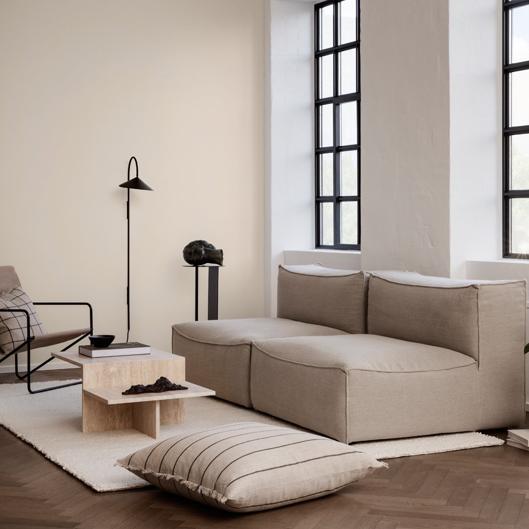 Beige sectional sofa with minimalist design, paired with a neutral-toned rug and striped pillow on dark wood floor.