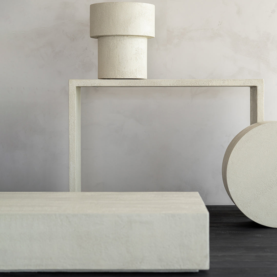 Minimalist beige decor featuring cylindrical and rectangular shapes against a soft gray wall and dark wood floor.