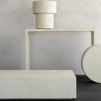 Minimalist beige decor featuring cylindrical and rectangular shapes against a soft gray wall and dark wood floor.