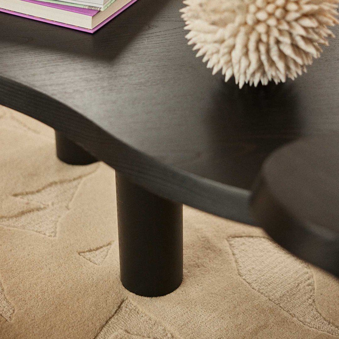 Black curved coffee table with smooth edges and round black legs, set against a textured beige rug.