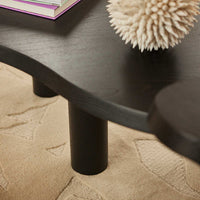 Black curved coffee table with smooth edges and round black legs, set against a textured beige rug.