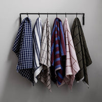 Assorted checkered towels in navy, white, pink, and green hues, displayed on a black hanger against a gray wall.