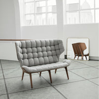 Gray tufted fabric loveseat with wood legs, set against a light gray floor and minimalist decor.