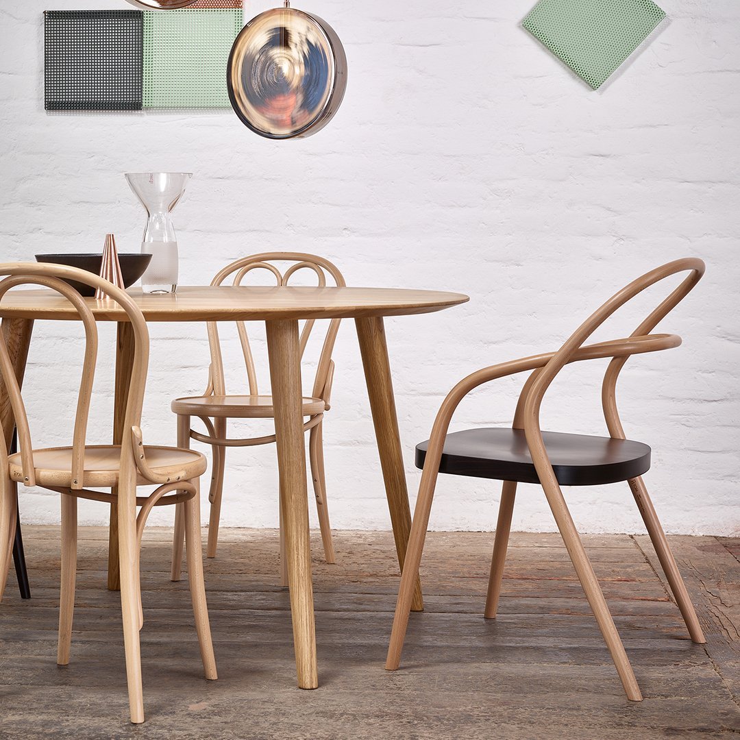 Natural wood dining table with light and dark wood chairs, set against a textured floor and minimalist wall decor.