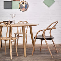 Natural wood dining table with light and dark wood chairs, set against a textured floor and minimalist wall decor.