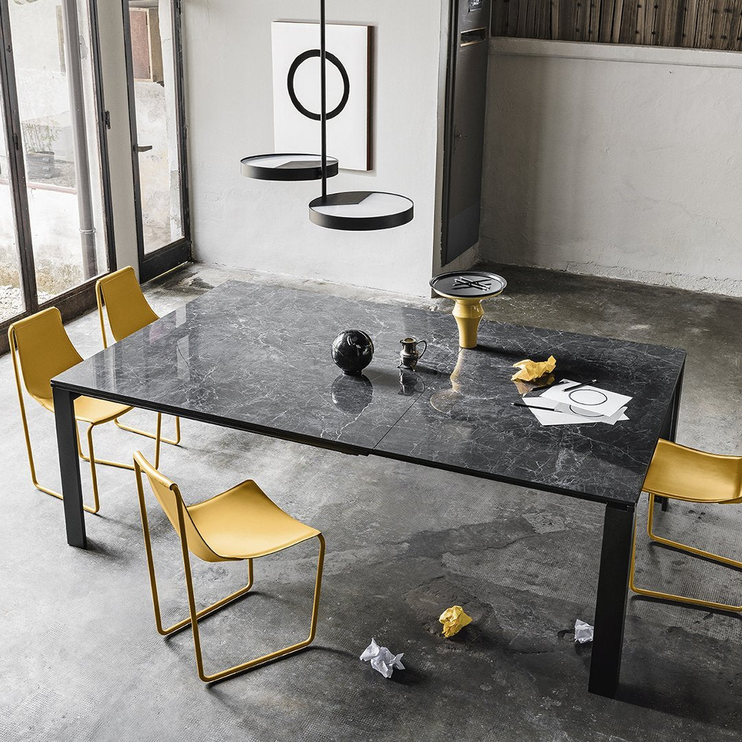 Modern black marble dining table with four yellow chairs, featuring a minimalist design and sleek finishes.
