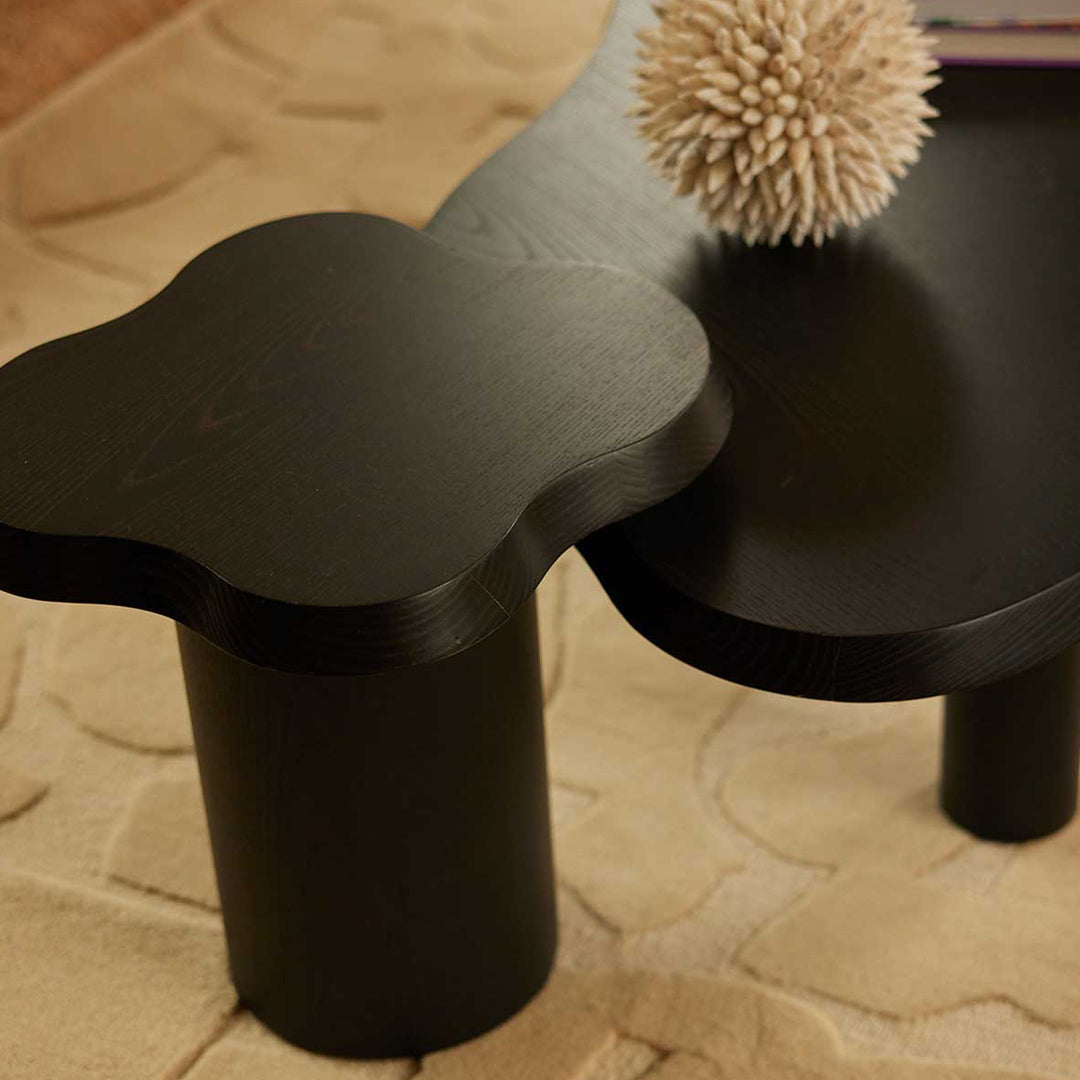 Black flower-shaped side table with sleek curves, paired with a soft beige rug. Elegant and modern design accents.