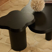 Black flower-shaped side table with sleek curves, paired with a soft beige rug. Elegant and modern design accents.