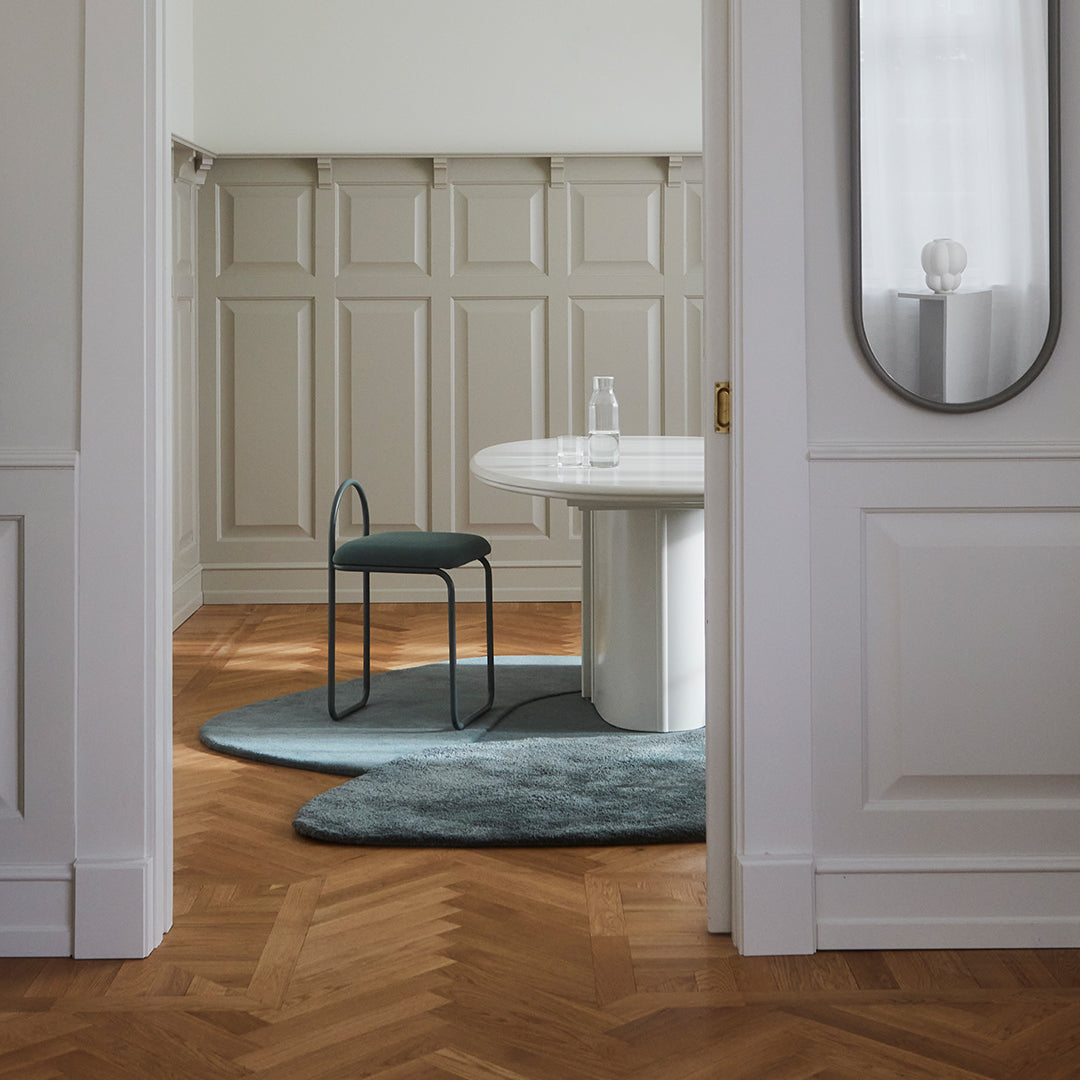 Elegant teal rug on warm brown herringbone floor, complemented by a minimalist white table and chair in a neutral interior.