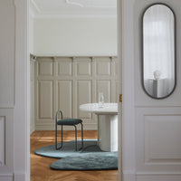 "Elegant teal chair with light gray walls and wooden herringbone floor, accented by a round white table and soft curves."