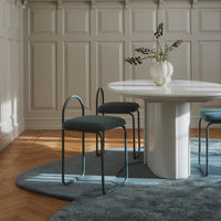 Round white table with teal chairs on a textured blue rug, set against a warm wooden floor and soft panelled walls.