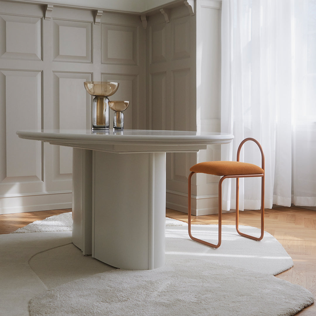 Modern round table in soft gray with a beige rug and a stylish orange chair, enhancing a minimalist aesthetic.