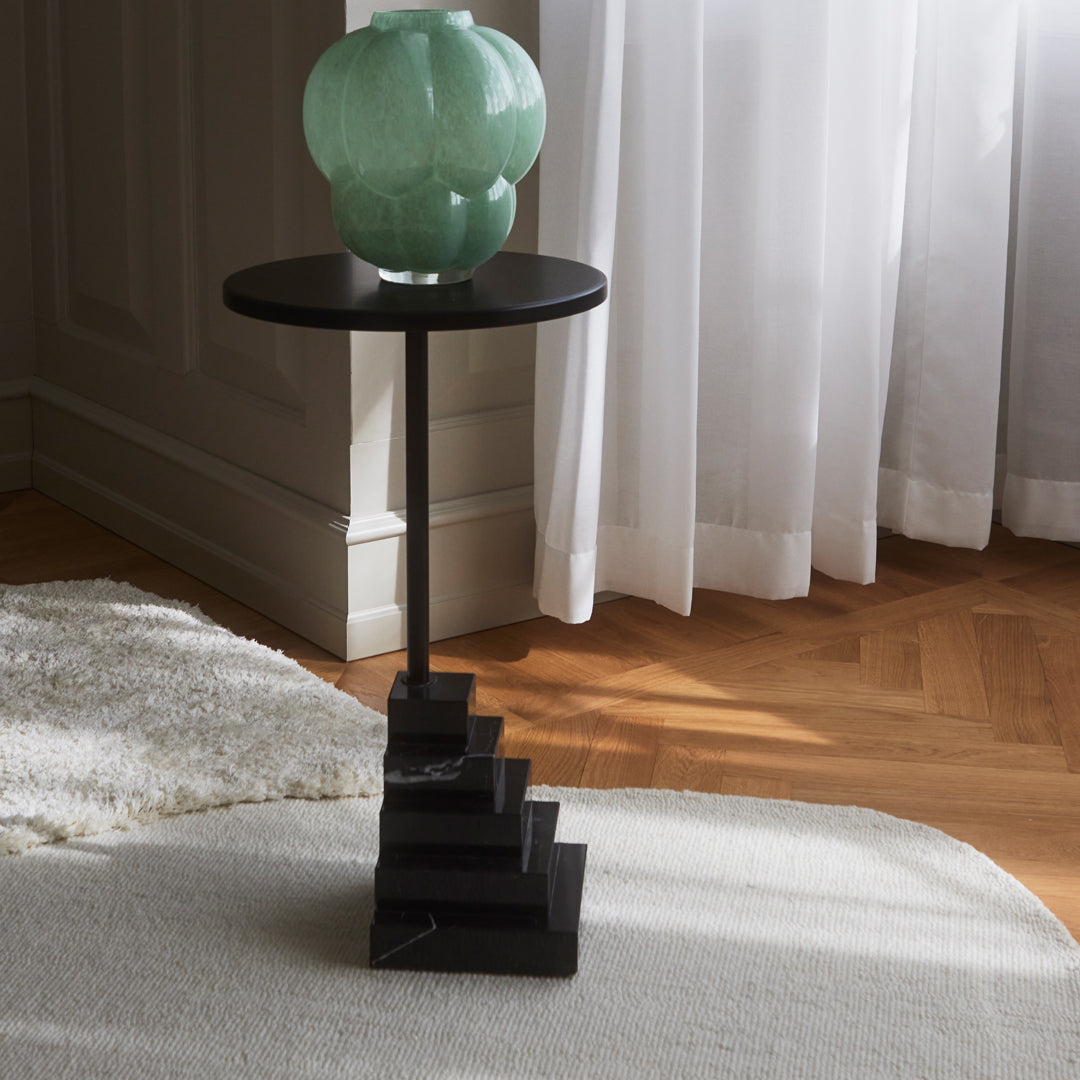 Black marble side table with a minimalist staircase design, topped with a soft green vase. Elegant and modern decor piece.