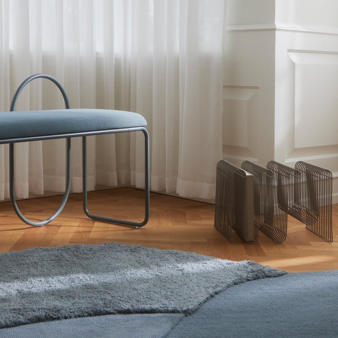 Blue upholstered chair with a sleek metal frame, alongside gray minimalist magazine holders on a warm wood floor.