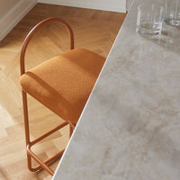 Orange upholstered chair with a curved metal frame, set against a marble tabletop and herringbone wood floor.
