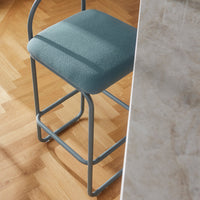 Light blue upholstered bar stool with a sleek metal frame, placed beside a marble countertop and wooden floor.