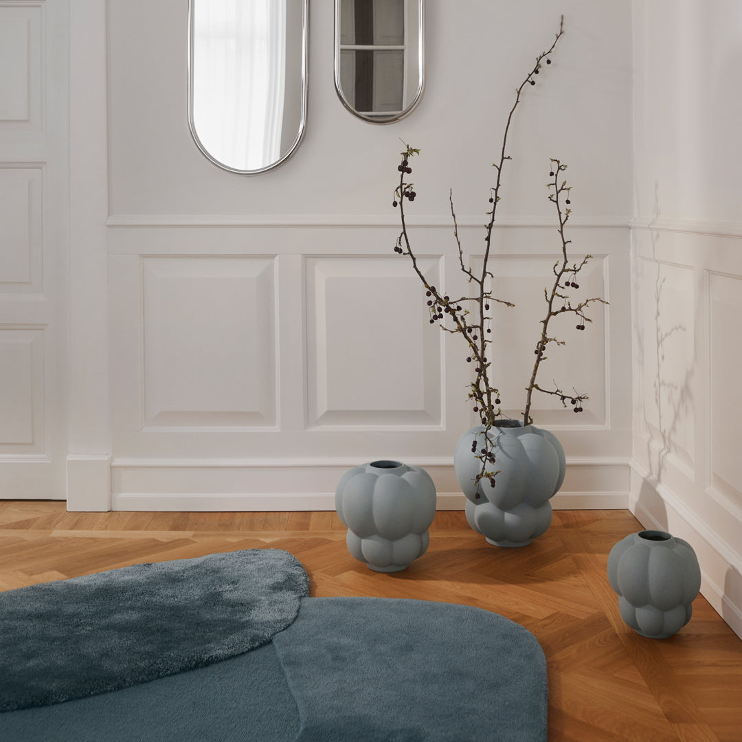 "Soft blue vases with organic shapes, accented by natural branches, set against a light wood floor and neutral wall."