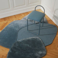 Soft blue abstract rug in organic shapes, paired with a sleek blue chair on warm wooden flooring.