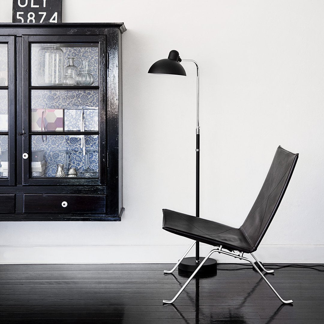 Sleek black chair with minimalist chrome frame, set against a crisp white wall and black wooden floor.