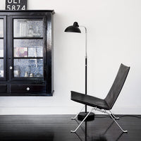Sleek black chair with minimalist chrome frame, set against a crisp white wall and black wooden floor.