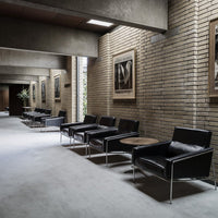 Sleek black leather chairs with chrome legs in a modern, minimalistic hallway setting against textured brick walls.