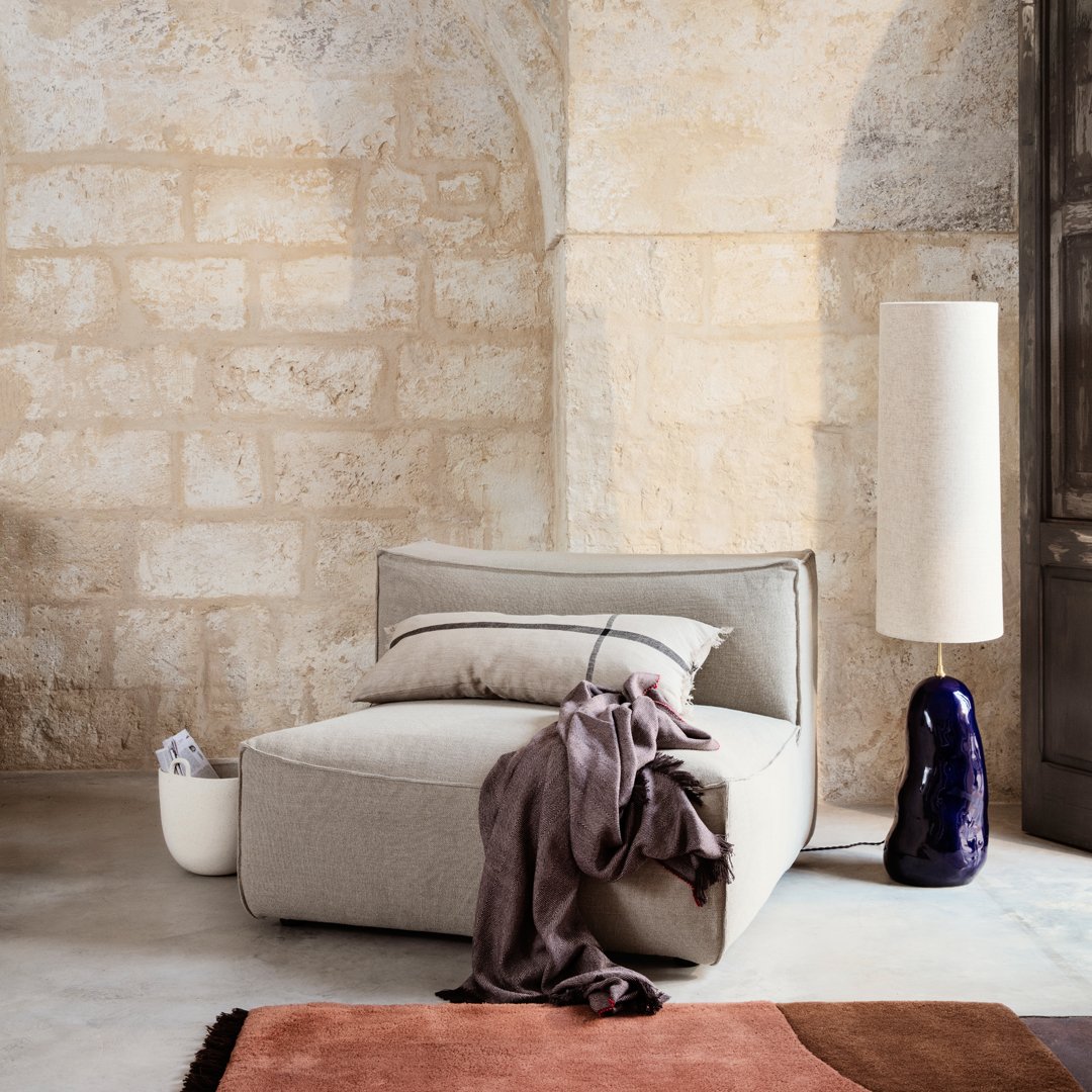 Cozy, light gray lounge chair with soft textures, paired with earthy tones and a smooth, dark blue lamp.