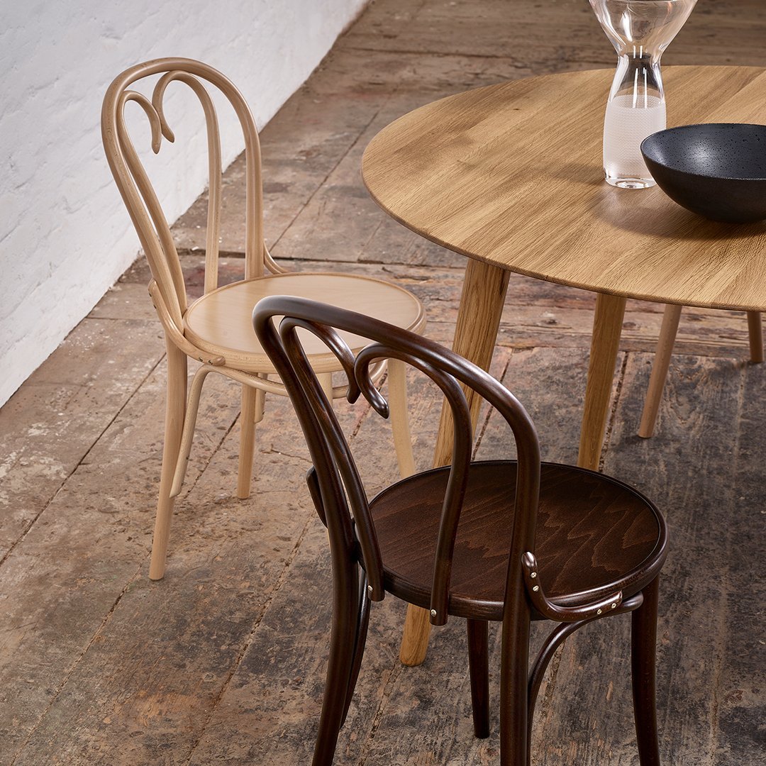 "Two stylish chairs in natural wood tones: light beige and dark brown, paired with a round wooden dining table."