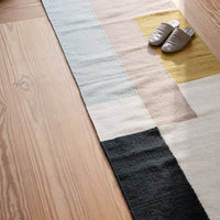 Colorful geometric rug featuring soft pastels, neutral tones, and bold black sections, perfect for modern decor.