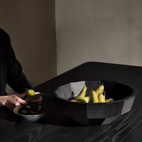 Black geometric bowl on a dark table, filled with vibrant yellow pears, creating a striking color contrast.