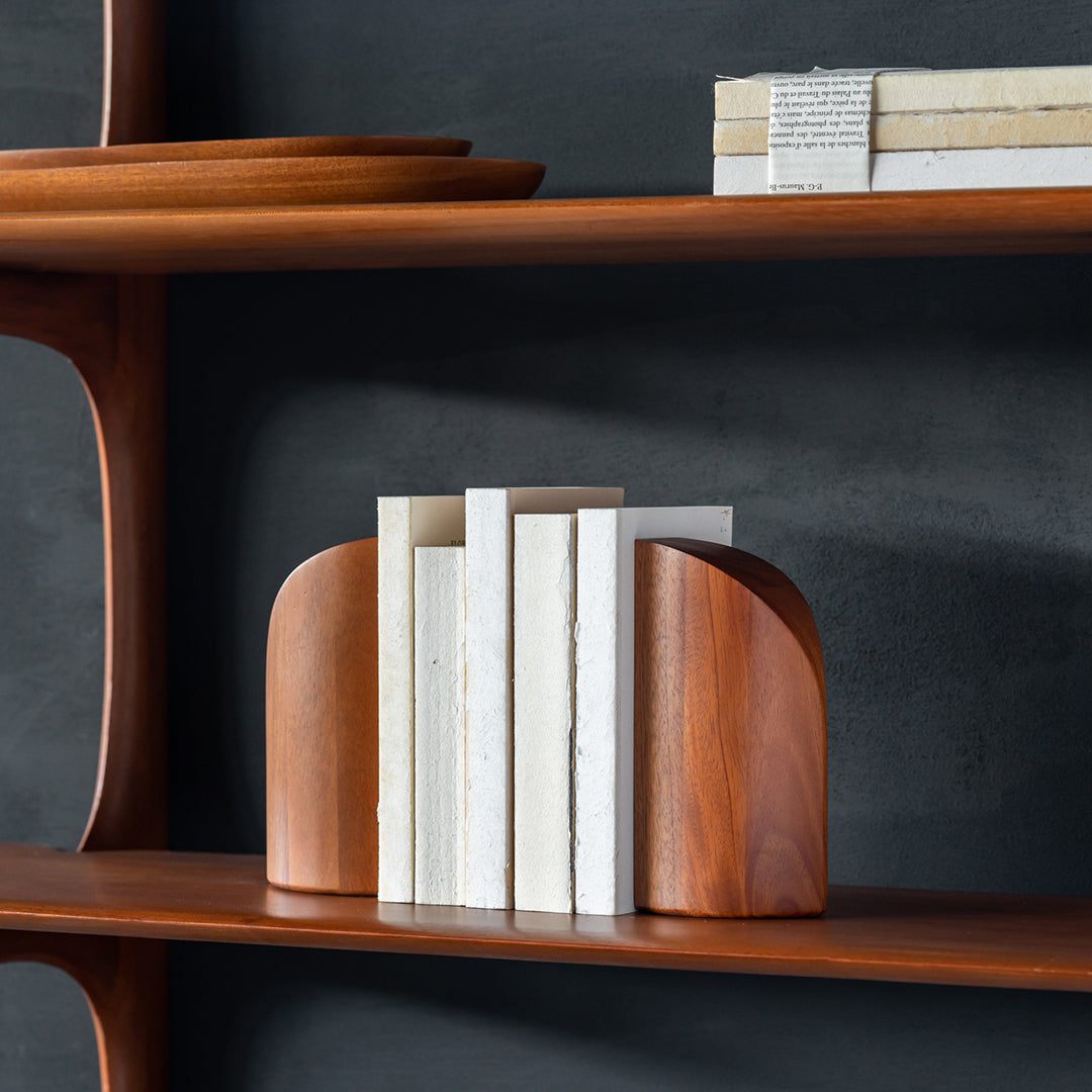 Wooden bookends in warm tones, featuring smooth curves and a mix of white and natural wood finishes on a dark shelf.