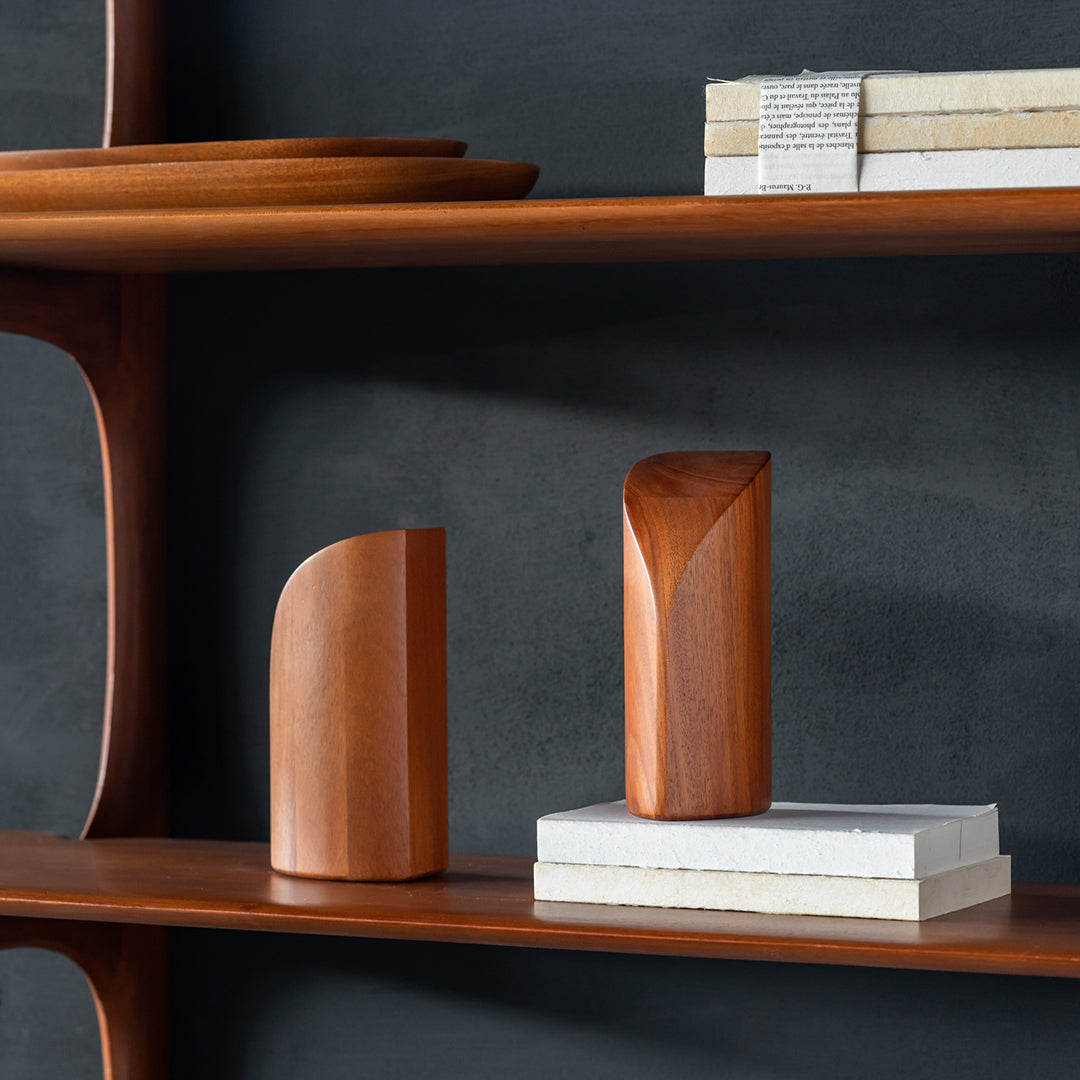 Wooden decorative pieces in rich brown hues with smooth, curved and angular designs on a minimalist shelf.