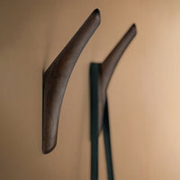 Dark wood wall hooks against a warm beige background, highlighting a smooth, minimalist design.
