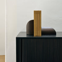 Modern black ribbed cabinet with a brown geometric decor and stacked golden books, offering a stylish contrast.