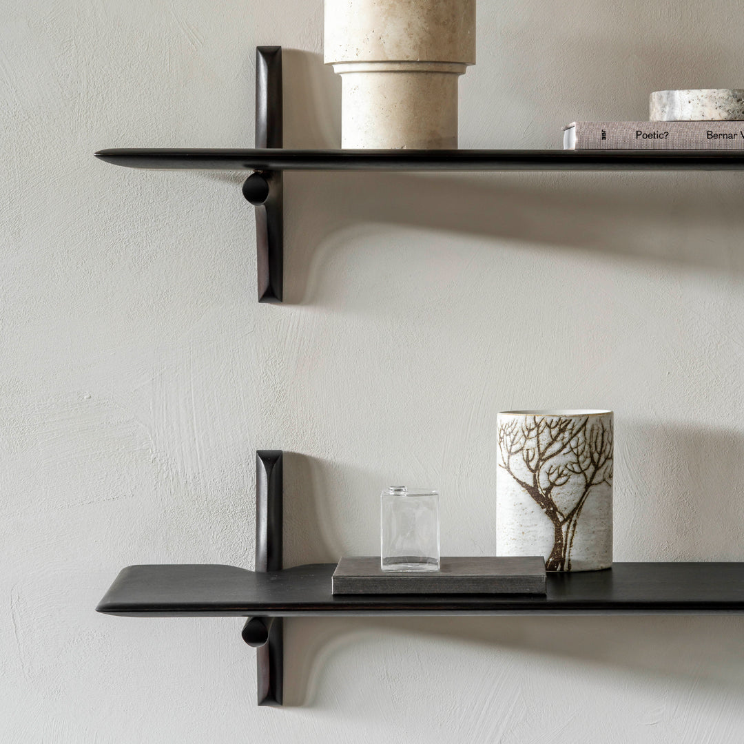 Black minimalist shelves against a textured light wall, featuring a ceramic vase and decorative items.