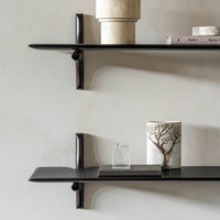 Black minimalist shelves against a textured light wall, featuring a ceramic vase and decorative items.
